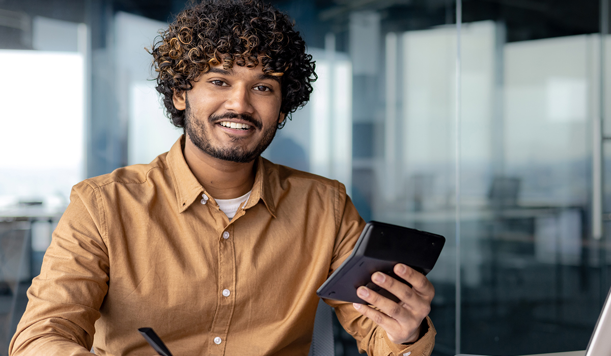 A smiling man works with a tablet at his desk in a contemporary office