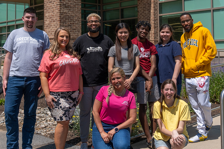 A group of diverse students and staff smiling together in front of a brick campus building.