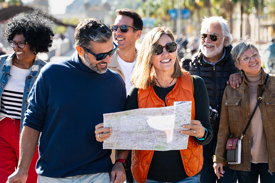 A diverse group of six adults smiling and looking at a paper map together outdoors on a sunny day, with palm trees visible in the background.
