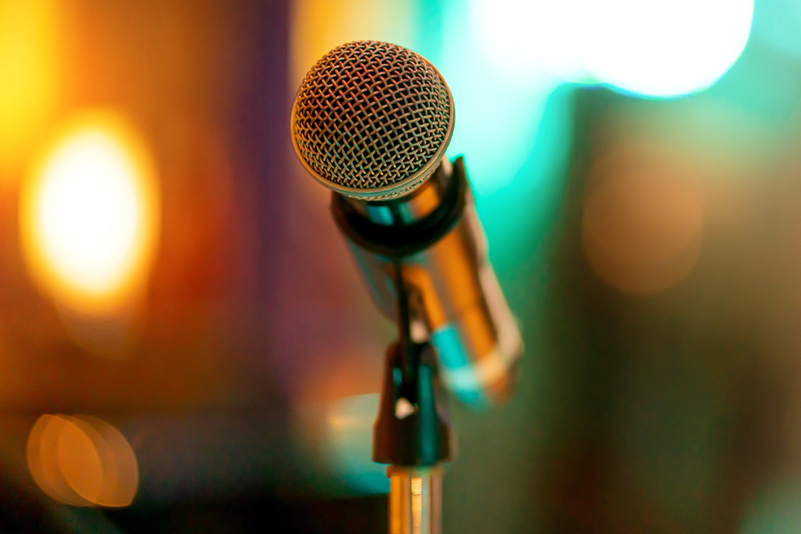 Close-up of a microphone on a stand with colorful stage lights blurred in the background.
