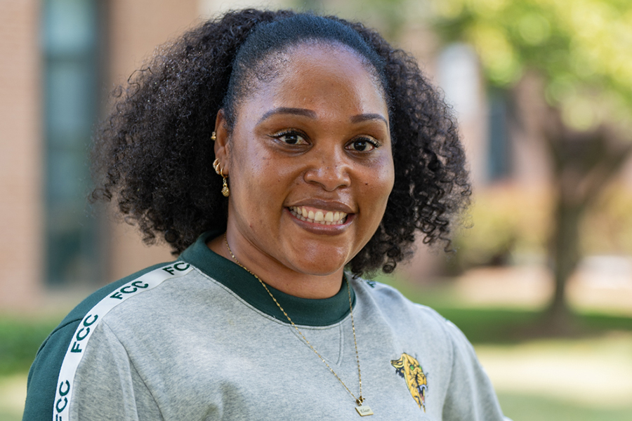 A close-up portrait of a smiling female student wearing a grey and green Frederick Community College sweatshirt outdoors.
