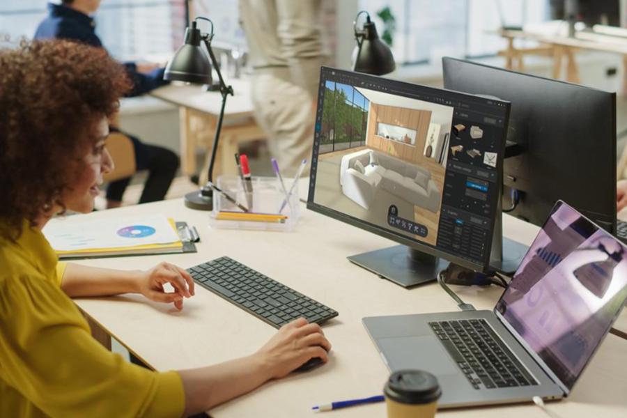 A female interior designer using 3D modeling software on a computer to design a living room layout.