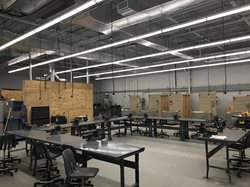 An industrial HVAC training lab featuring large work tables with vices and several wooden training stalls or workstations in the background under bright fluorescent lighting.
